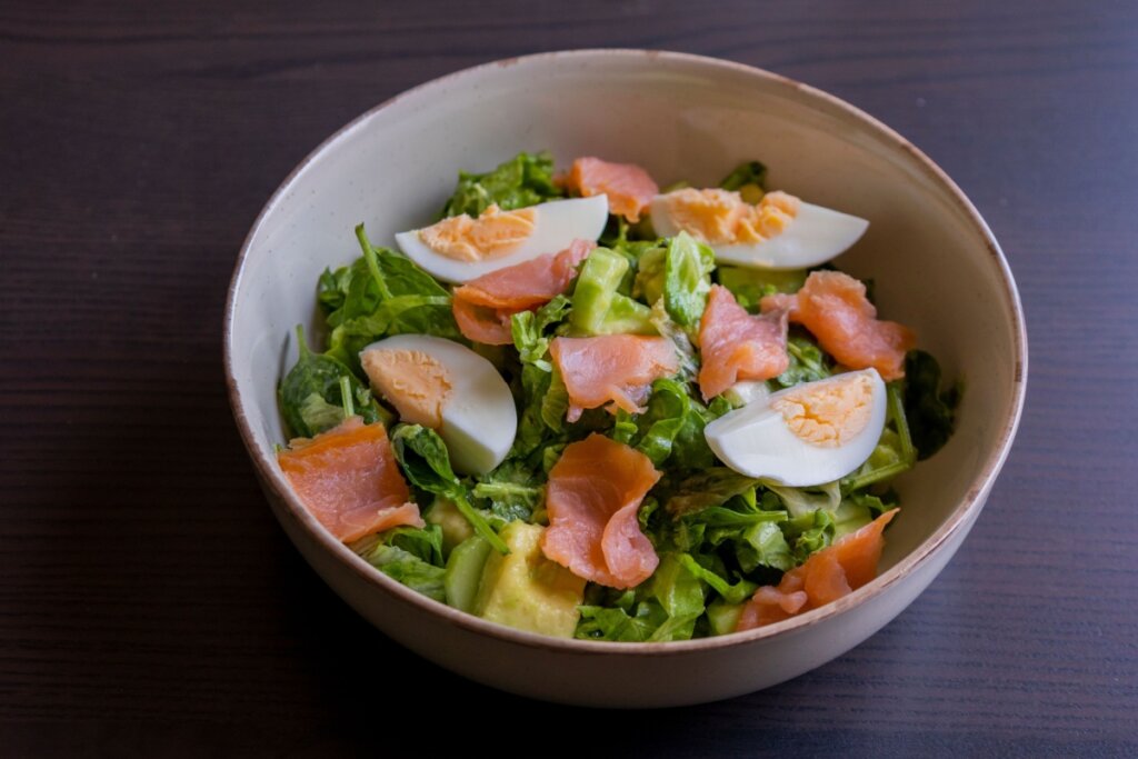 Recipiente branco com salada com salmão, ovo e abacate