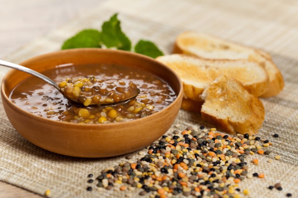 Sopa de lentilha mista em um recipiente marrom com fatias de pão tostadas ao lado