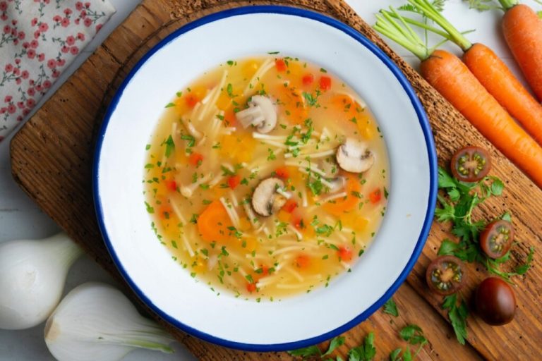 Sopa de macarrão com legumes e cogumelos em prato branco com borda azul
