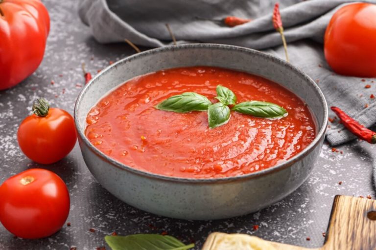 Creme de tomate com folha de manjericão servido em tigela de cerâmica cinza em cima de mesa de pedra
