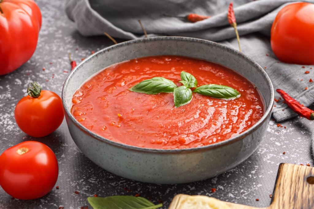Creme de tomate com folha de manjericão servido em tigela de cerâmica cinza em cima de mesa de pedra