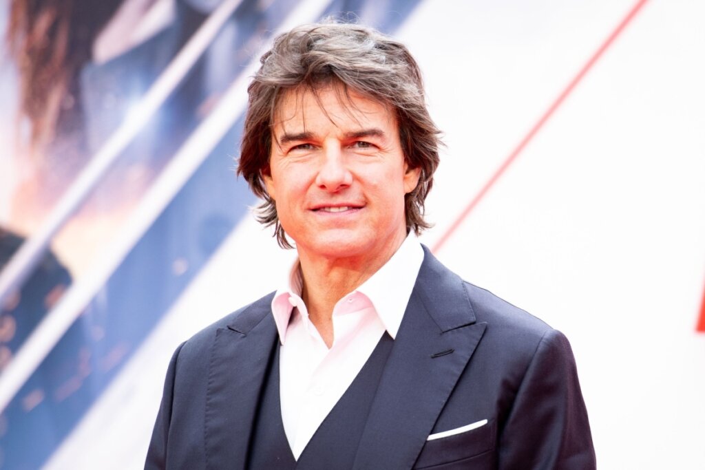 Homem com o cabelo curto escuro, usando camisa social branca e terno preto posando para foto