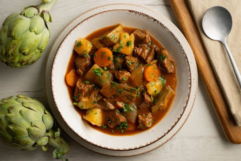 Prato branco com ensopado de carne com alcachofra, batatas e cenouras