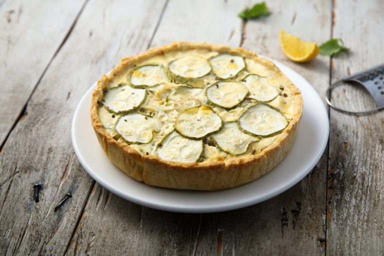 Torta de abobrinha com castanha-de-caju em prato branco em cima de mesa de madeira