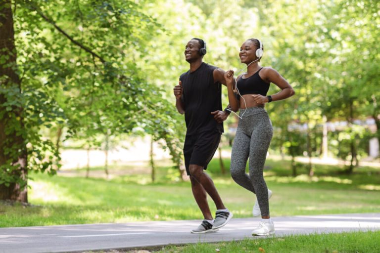 Casal correndo em parque com fones de ouvido e sorrindo