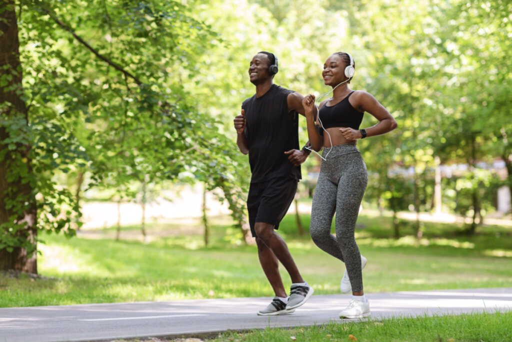 Casal correndo em parque com fones de ouvido e sorrindo