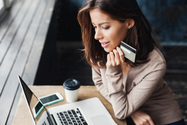 Mulher sentada mexendo em notebook e segurando um cartão de crédito
