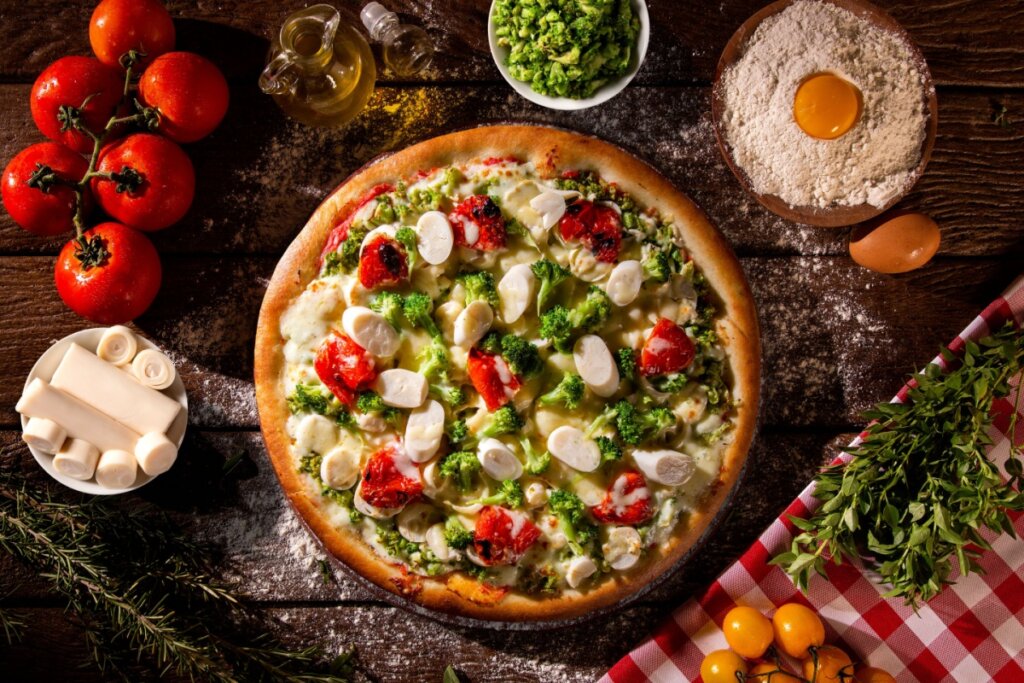 Pizza de palmito com brócolis e tomate em cima de uma mesa de madeira enfarinhada com farinha de trigo