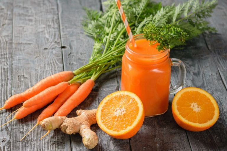 Suco laranja em copo de vidro com cenouras, laranja e gengibre em volta