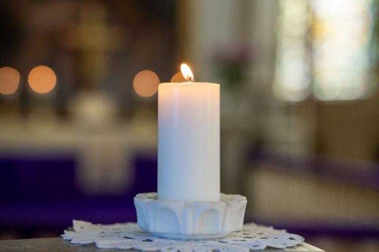 Imagem de uma vela branca acesa em cima de  um recipiente de vidro 